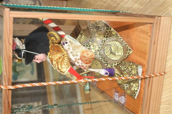 A Japanese wooden cased model of a Samurai warrior holding aloft a fan, with ornate silkwork robes, overall height 35cm, width 33cm